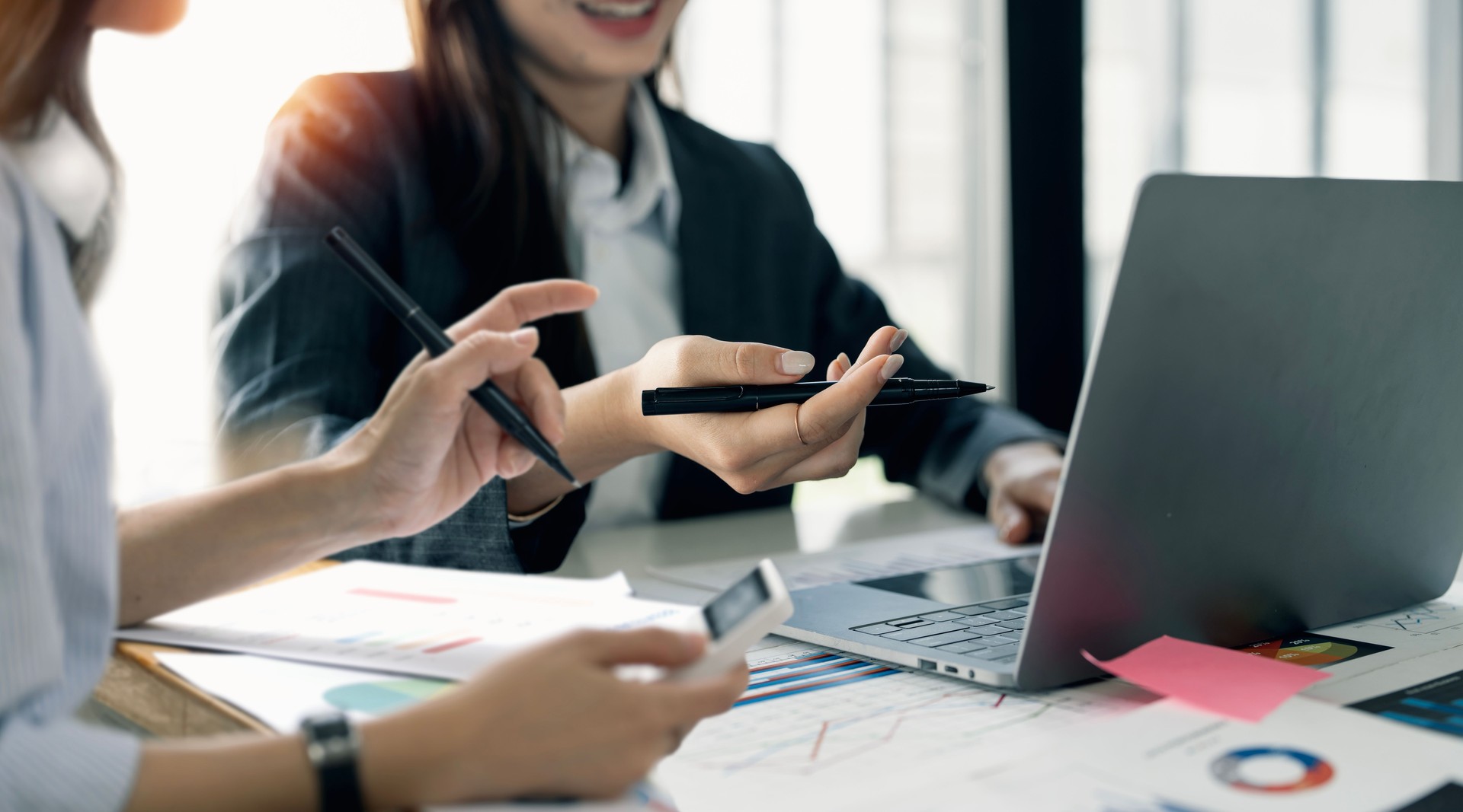 Teamwork of asian businesswoman discussing and calculating on evaluation data in conference room, pointing to the chart graph on laptop computer.