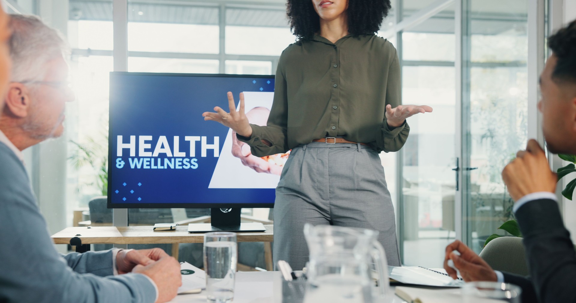 Presentation, health and wellness with screen at office, hands or talk with advice, info or pitch. Person, speaker and audience with monitor, discussion and employee wellbeing in boardroom at agency